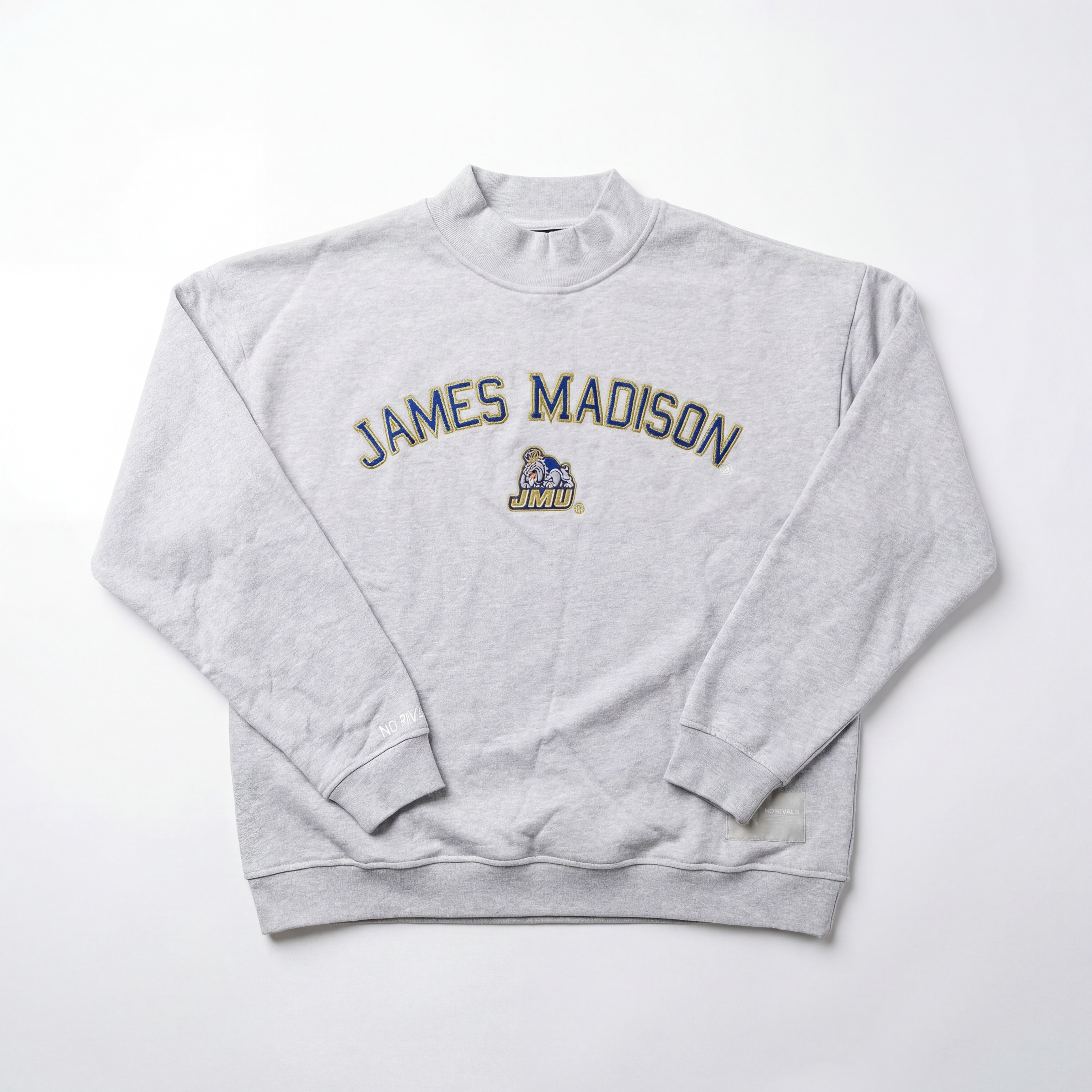 The No Rivals JMU Mock Neck is a light gray, oversized crewneck sweatshirt featuring “JAMES MADISON” in large letters across the chest and a cartoon bulldog mascot above “JMU” at the center.