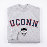 A folded gray UConn Mock Neck sweatshirt by No Rivals, featuring "UCONN" in large navy and red letters with a husky face logo below the text. Made from heavyweight cotton, one sleeve is neatly folded over the front.