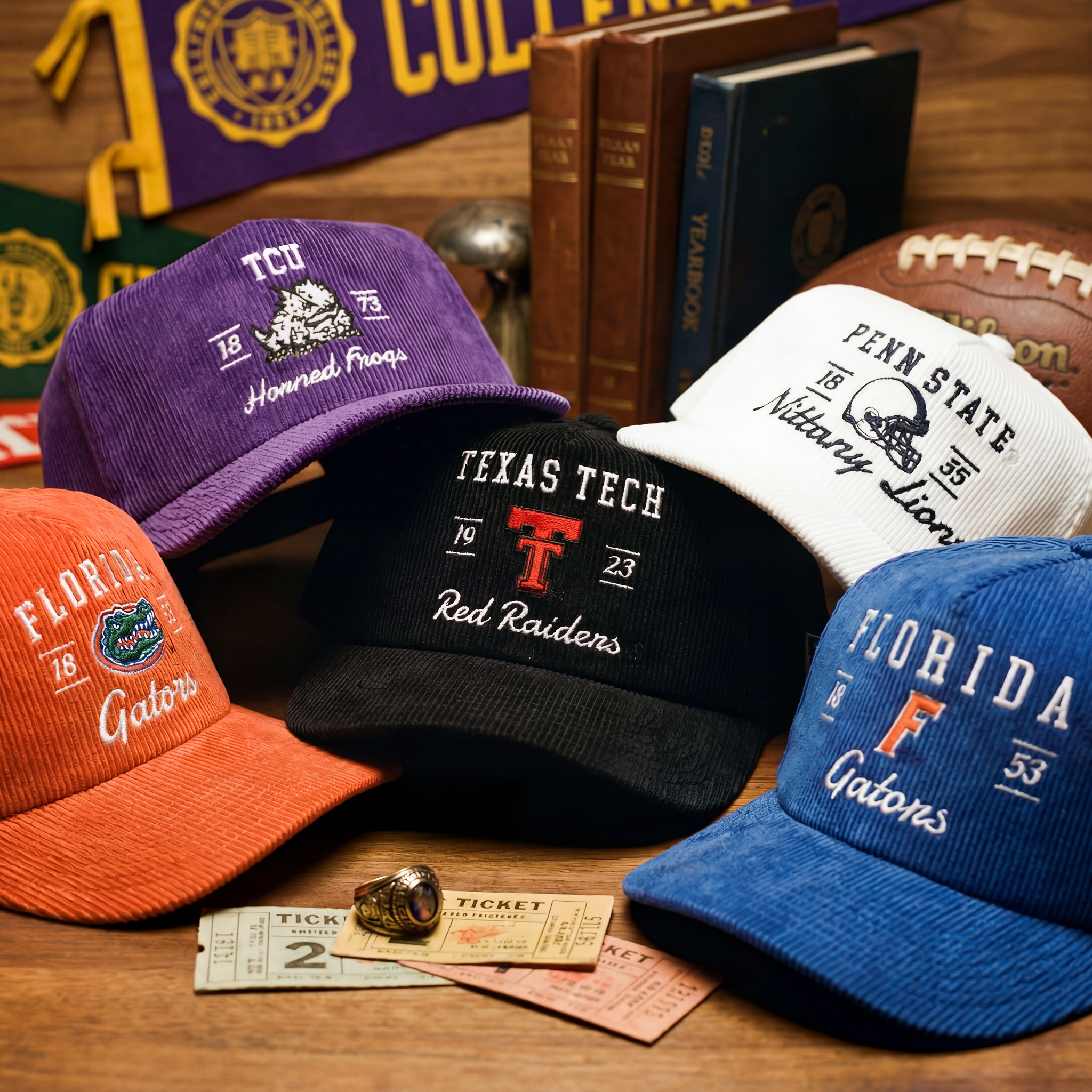 Five embroidered college caps—TCU (purple), Penn State (white), Texas Tech (black), Florida Gators (orange and blue)—are displayed with vintage tickets, books, a football, and school memorabilia in the background.