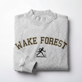 A folded light gray Wake Forest Mock Neck by No Rivals, crafted from heavyweight cotton, features bold black and gold WAKE FOREST lettering with the Demon Deacons mascot below and “NO RIVALS” text on the left sleeve.