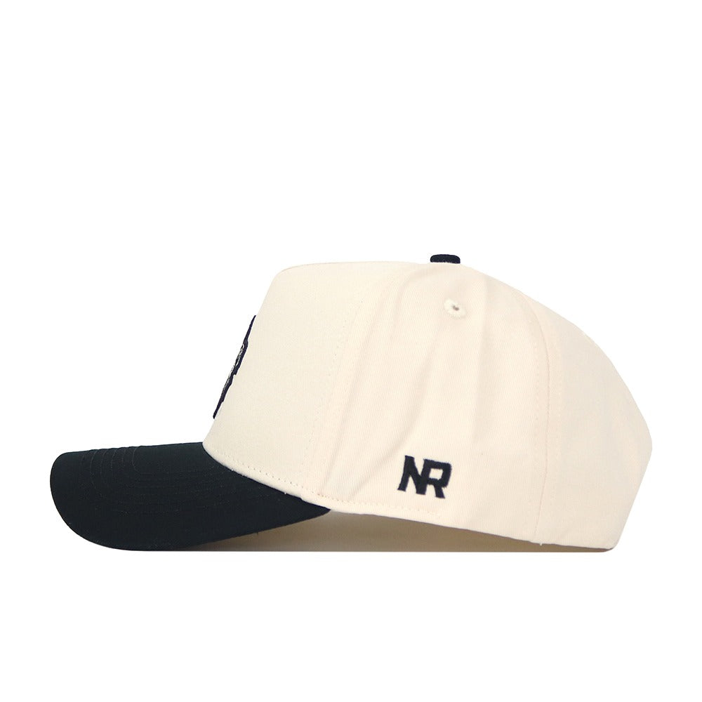 The Georgia Vintage Logo Patch Hat - Classic Black is a cream-colored cap with a black brim, viewed from the side. Made from quality cotton, it offers a structured fit and showcases NR initials in black near the back.