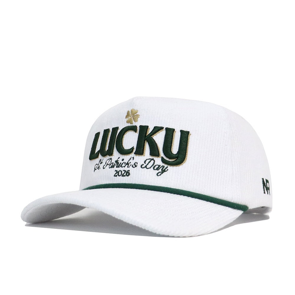The No Rivals St.Pattys Lucky Cord Hat in white features green and gold "LUCKY" with a shamrock, "St. Patrick’s Day 2026" embroidery, a green-accented brim, unstructured fit, and a small '47 logo on the side.