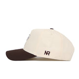 The No Rivals University of Kansas Espresso Hat is a cream snapback with a dark brown curved brim and NR initials embroidered in brown on the side, made from premium cotton. It has a structured fit and is displayed from a side angle on a white background.