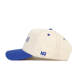 The University of Kansas Vintage Hat by No Rivals is cream-colored with a blue brim and blue NR initials on the side, made from high quality cotton. Officially licensed, it's shown in a side view against a white background.