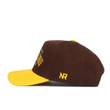 The Wyoming Wrestling Hat from the No Rivals Takedown Collection features brown cotton, a yellow brim, and yellow NR initials on the side—shown in profile and perfect for fans of the classic dad hat style.