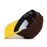 The No Rivals Wyoming Wrestling Hat from the Takedown Collection is shown upside down, revealing its black and white cotton inner lining with NO RIVALS printed inside. The snapback features a yellow brim and a brown body.