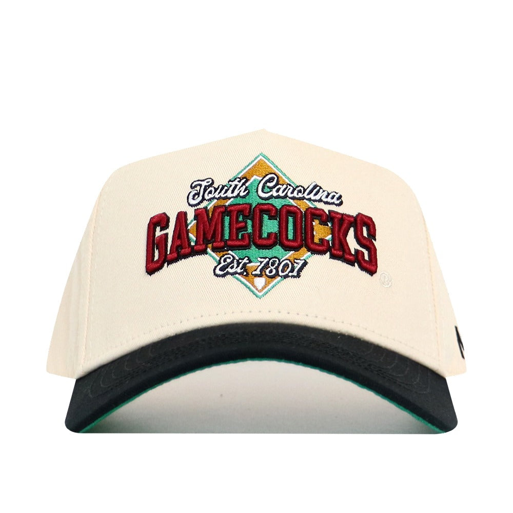 The No Rivals South Carolina Ballpark Hat is a white snapback with "South Carolina GAMECOCKS Est. 1801" embroidered in red, green, and gold on the front, featuring a black curved brim and structured cotton fit.