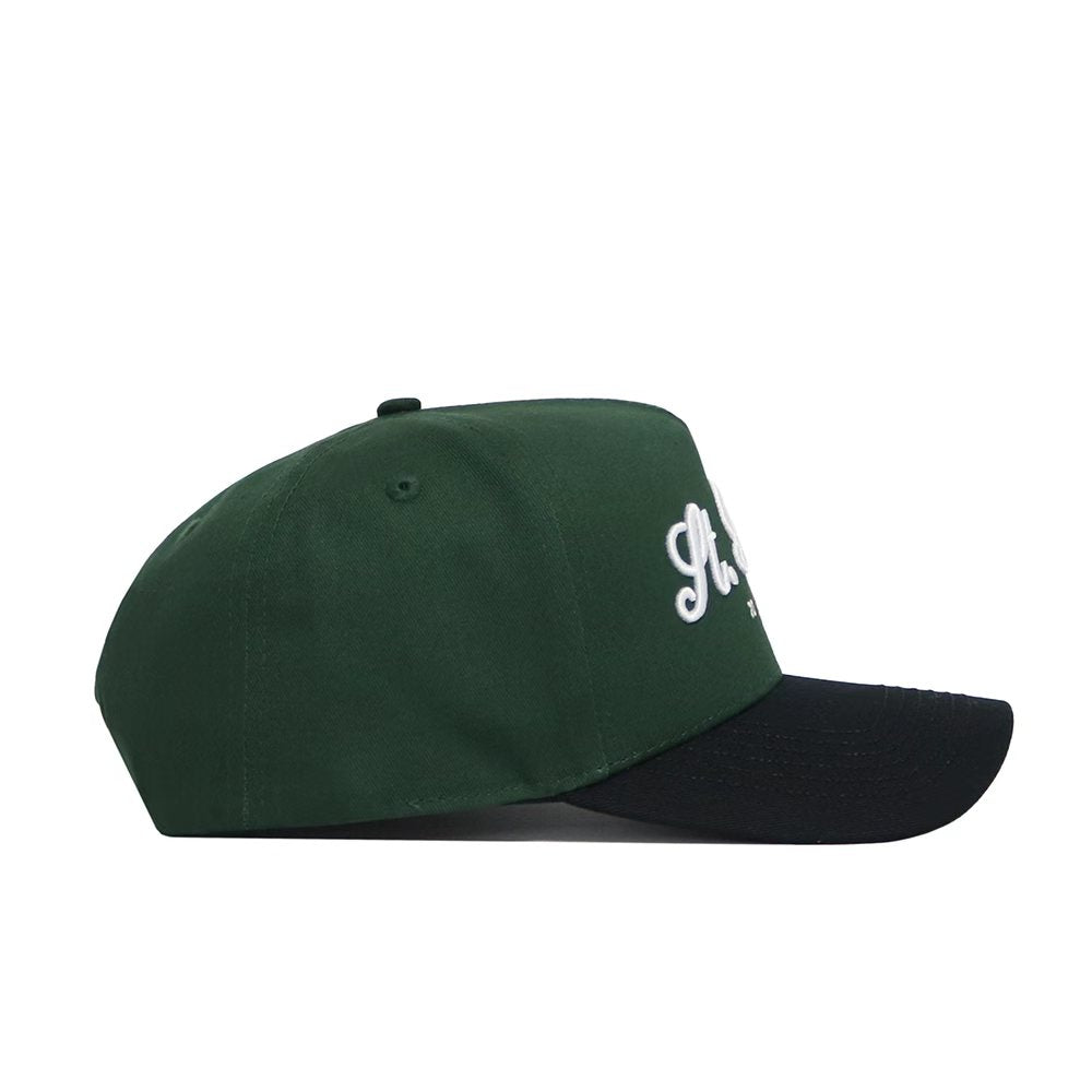 The No Rivals St.Pattys Shamrock Hat is a green corduroy cap with a black brim, shown from the side. Partially visible white embroidered text appears on the front. Unstructured fit offers casual comfort.