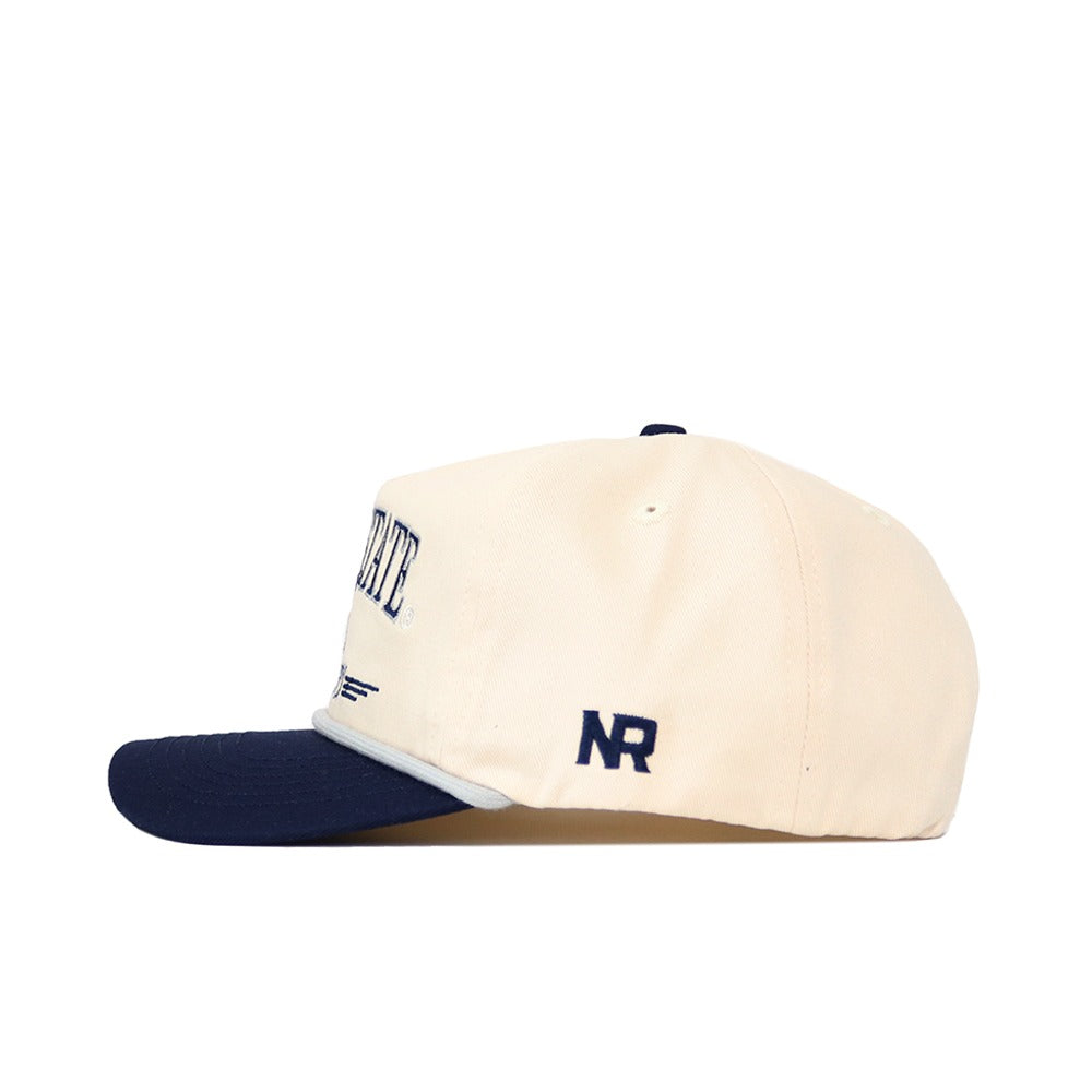 The No Rivals Penn State Hockey Hat is a cream cotton baseball cap with a navy bill, NR embroidered on the side, partial front logo visible from the side, and a classic snapback closure.