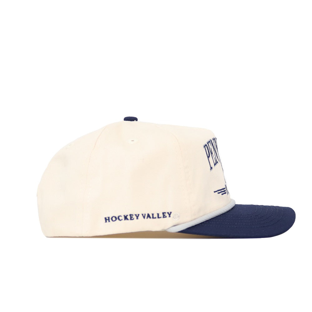 The Penn State Hockey Hat by No Rivals is a cream cotton cap with a navy blue brim and button. "HOCKEY VALLEY" is embroidered on the side. This officially licensed hat is pictured in a side profile view.