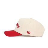 The Upside Down Ball State Hat by No Rivals is a cream snapback with a red brim, red embroidered front text, and NR stitched on the side. Made of high quality cotton, this structured cap is shown in side profile on a white background.