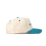 The No Rivals UNC Wilmington Vintage Hat is a cream snapback with a teal brim, button, and stitching. Made from premium cotton for a structured fit, it displays partial teal text on the side against a white backdrop.