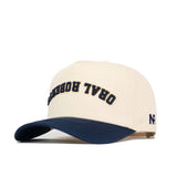 The Upside Down Oral Roberts Hat by No Rivals features beige cotton with a navy brim, "ORAL ROBERT" embroidered in reversed navy text on the front, and "NR" stitched on the left side of this structured snapback.