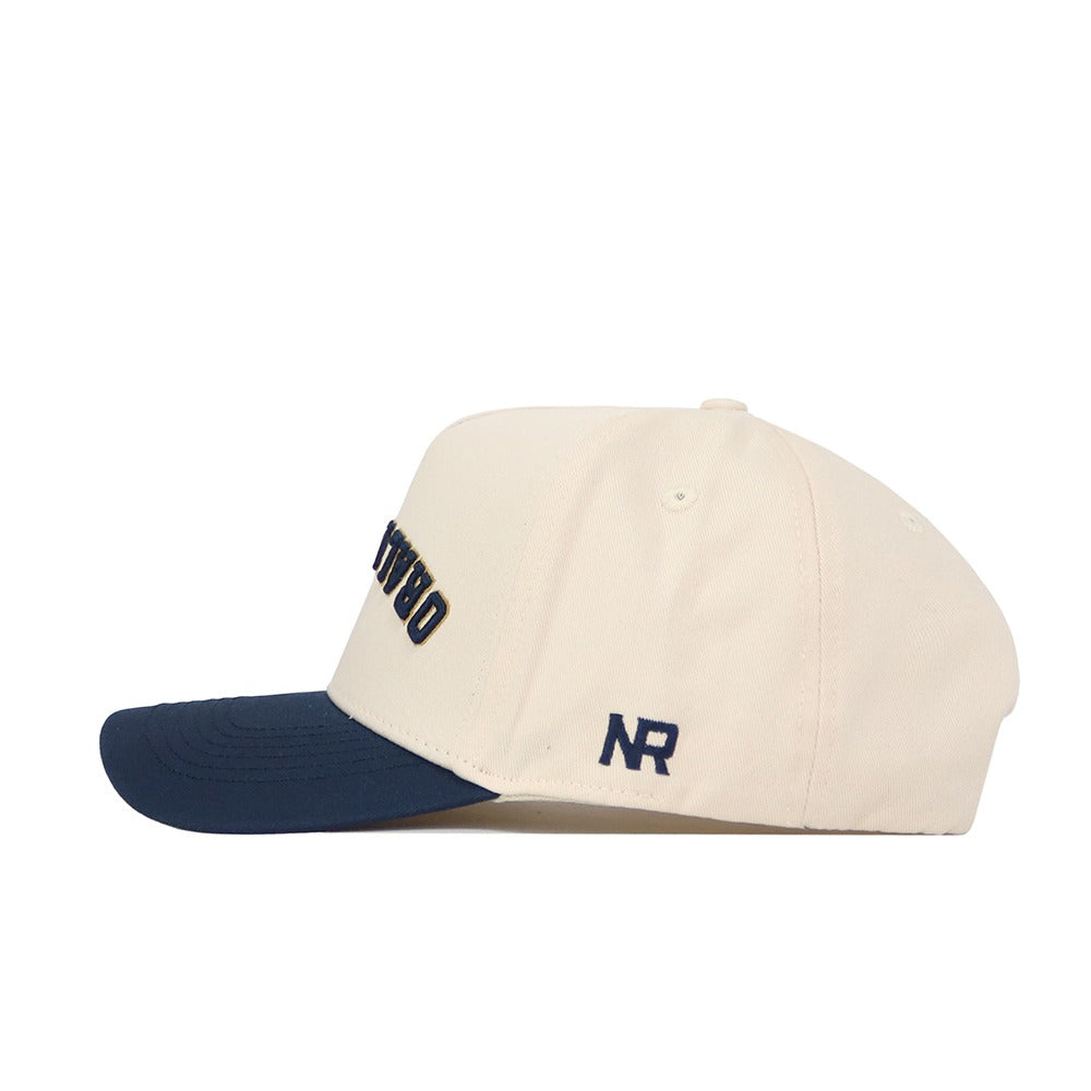 The Upside Down Oral Roberts Hat by No Rivals features classic colors: a cream crown, navy blue brim, and embroidered NR initials. Made from quality cotton with a structured fit and adjustable snapback for comfort.