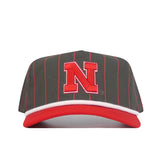 The Nebraska Gray Unstructured Hat by No Rivals features a gray design with thin red vertical stripes, a bold red "N" outlined in white on the front, and a red-and-white brim, crafted from high-quality cotton.