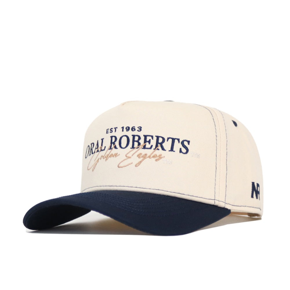 The Oral Roberts Vintage Hat by No Rivals is a beige and navy snapback cap made from high-quality cotton, featuring "ORAL ROBERTS Golden Eagles EST 1963" on the front and an OR logo on the side.
