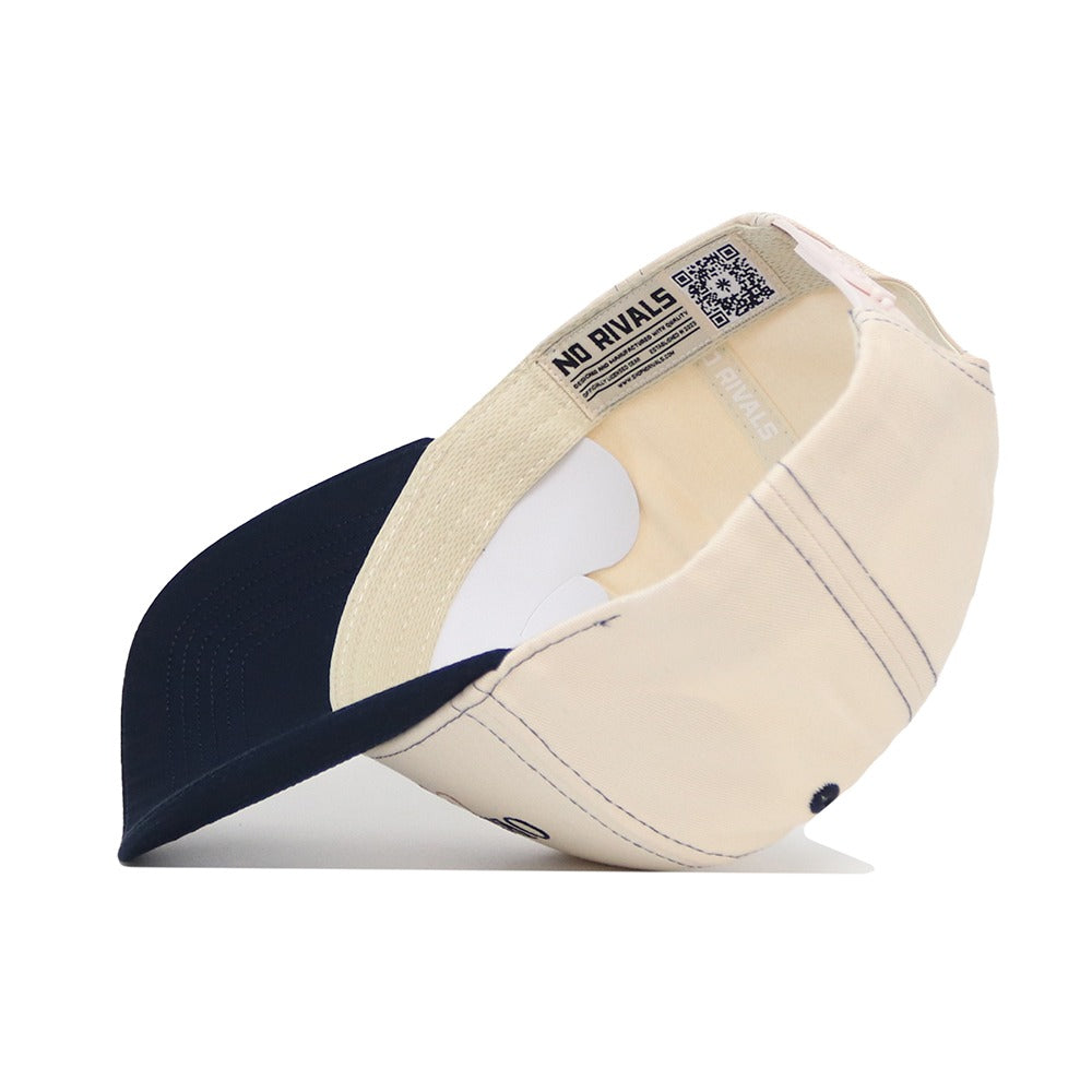 The Oral Roberts Vintage Hat by No Rivals is shown inside out, revealing stitching details, interior labels, and a QR code on the inner band. This beige and navy snapback features a navy brim and is made from high-quality cotton.