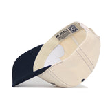 The Oral Roberts Vintage Hat by No Rivals is shown inside out, revealing stitching details, interior labels, and a QR code on the inner band. This beige and navy snapback features a navy brim and is made from high-quality cotton.