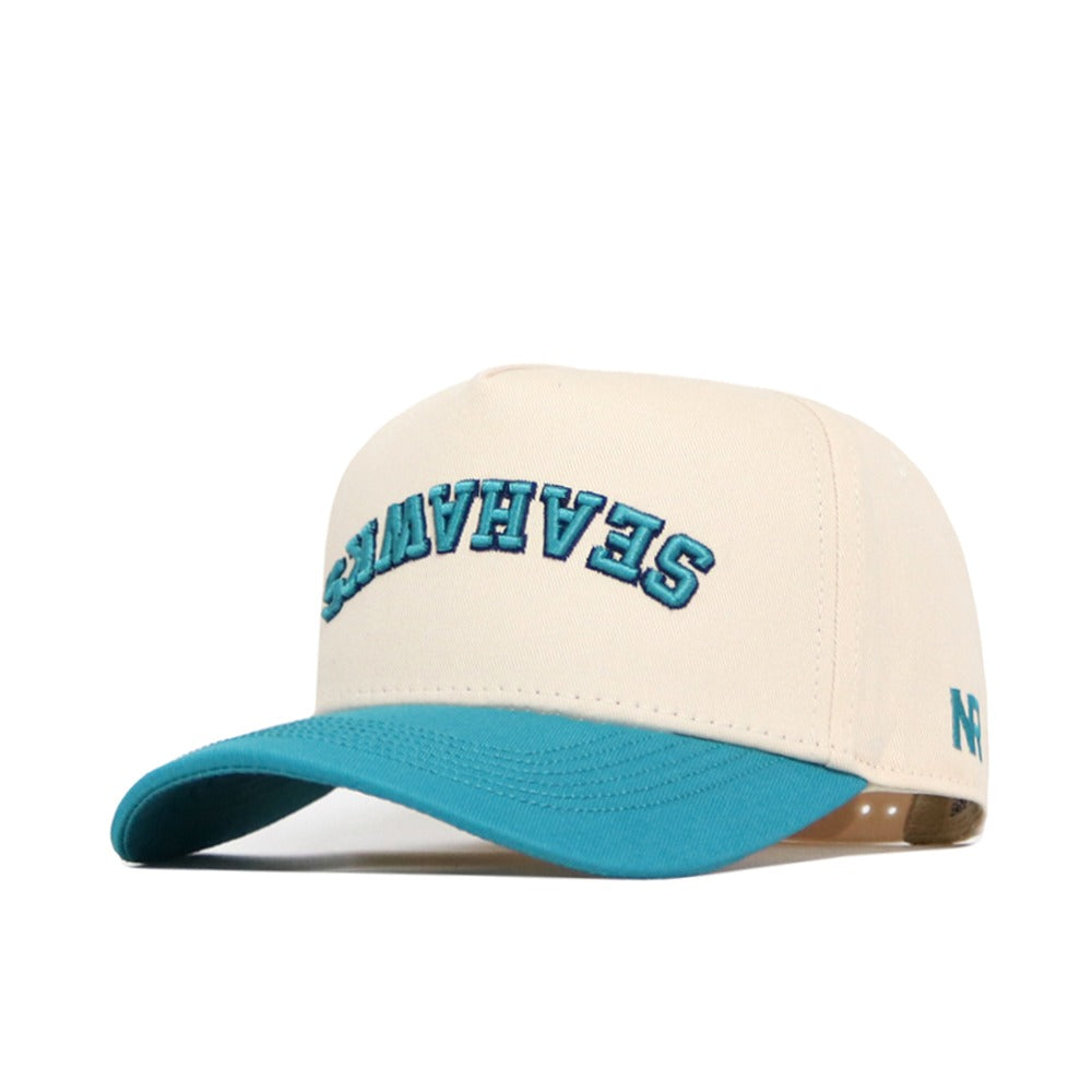 The No Rivals Upside Down Seahawks Hat - UNCW - Classic Colors features a cream cap with teal brim, "SEAHAVEN" embroidered upside down in teal with blue outline, structured fit, and small blue logo on the left side. High quality cotton.