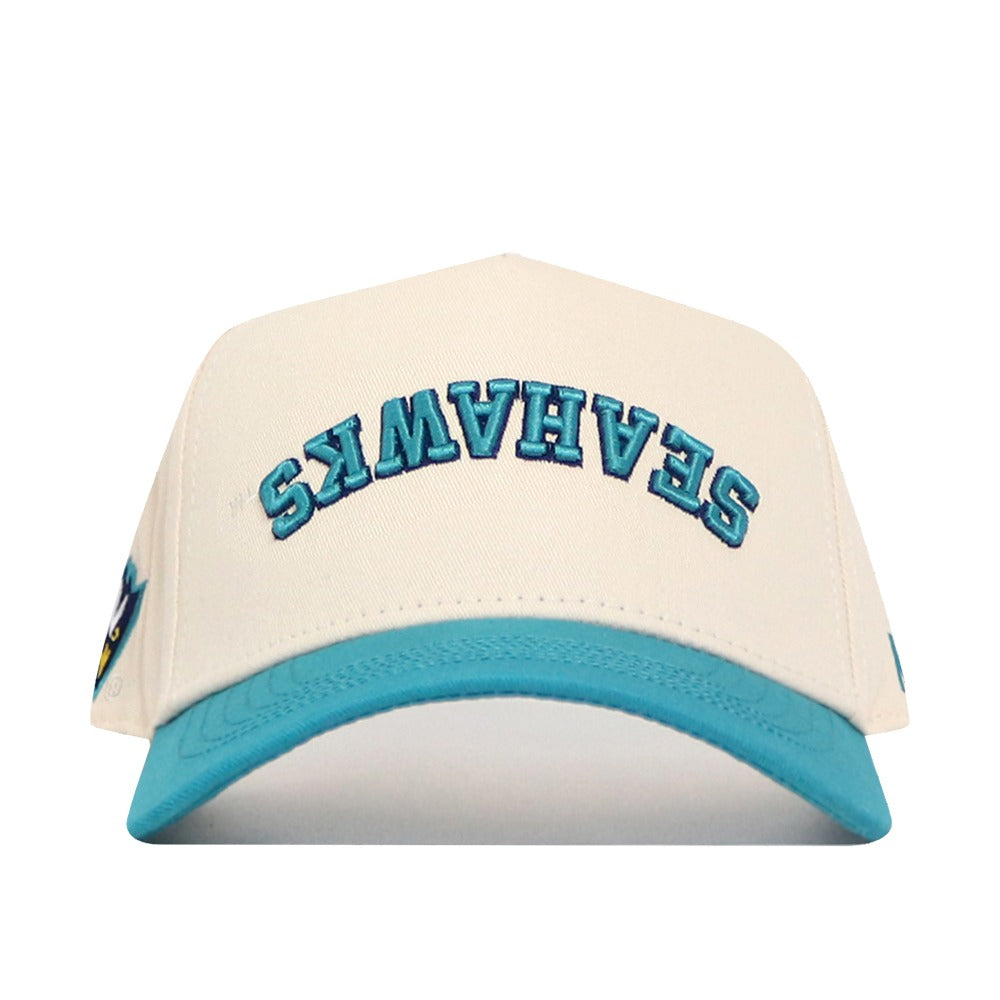 The No Rivals Upside Down Seahawks Hat - UNCW - Classic Colors features a cream snapback, turquoise brim, and blue SEAHAWKS lettering flipped on the front. Made from high-quality cotton for a comfortable, structured fit.