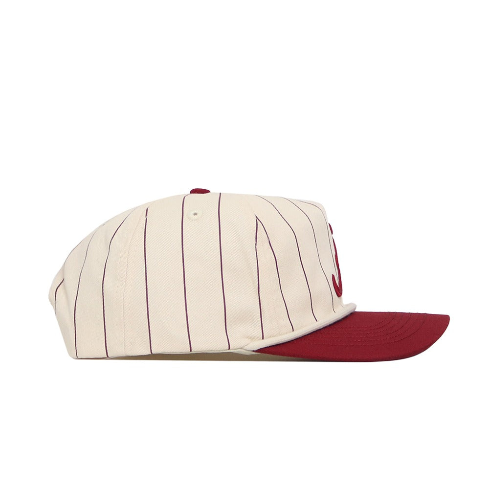 The Alabama Pinstripe Hat by No Rivals is a cream baseball cap with maroon pinstripes and a solid maroon brim, made from soft cotton with a snapback closure, shown from the side.