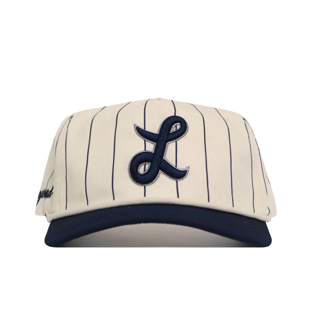 The No Rivals Longwood Pinstripe Hat features a cream base with thin black vertical stripes, a bold navy embroidered cursive L on the front, navy brim, and an adjustable snapback closure for a perfect fit.