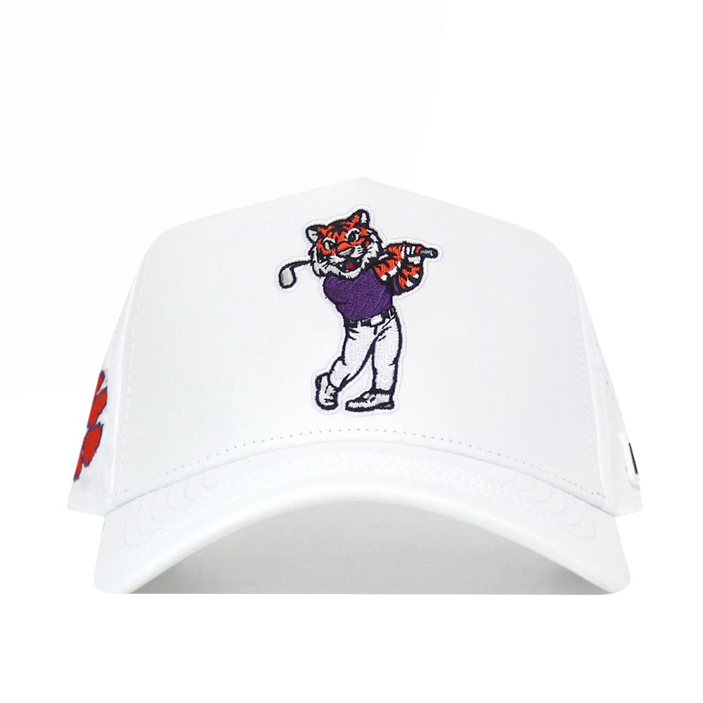 The Clemson Golf Hat - Swinging - White by No Rivals features an embroidered cartoon tiger in a purple shirt and white pants swinging a golf club on the front, with an orange paw print accent on the left side. This white baseball cap offers a comfortable snapback closure for an adjustable fit.
