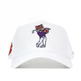 The Clemson Golf Hat - Swinging - White by No Rivals features an embroidered cartoon tiger in a purple shirt and white pants swinging a golf club on the front, with an orange paw print accent on the left side. This white baseball cap offers a comfortable snapback closure for an adjustable fit.