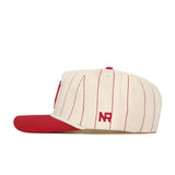The Indiana University Pinstripe Hat by No Rivals features a cream base with red pinstripes, a red brim, and the “NR” logo embroidered in red on the side. This unstructured cap has a snapback closure for an adjustable fit and is displayed from the side against a plain white background.