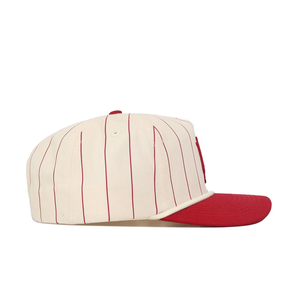 The No Rivals Indiana University Pinstripe Hat is displayed from the side against a white background, showcasing its cream color with thin red vertical pinstripes and a solid red brim. This hat features an unstructured fit and a snap back closure for adjustable sizing.