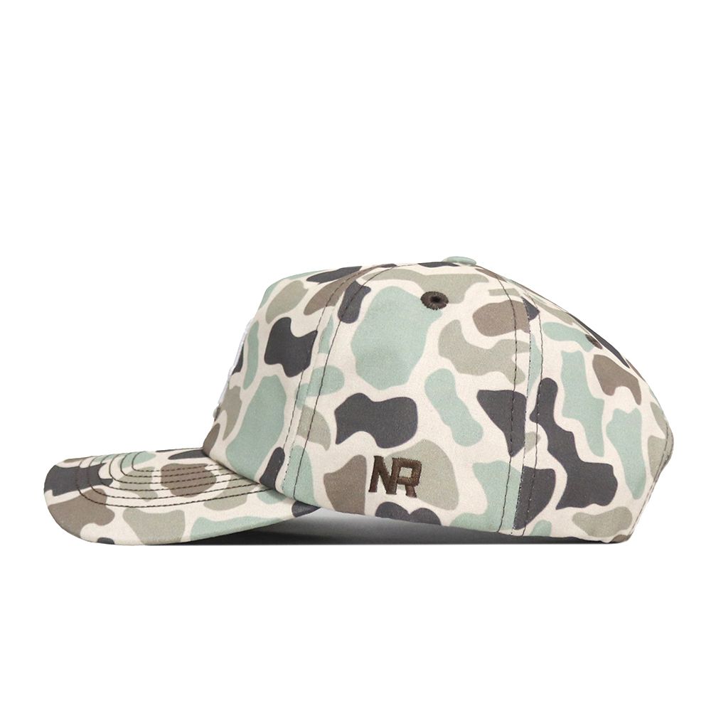The Alabama Crimson Tide Huntsman Hat by No Rivals features a camouflage pattern in shades of green, beige, and black, crafted from high-quality cotton and accented with the embroidered letters “NR” on the side.