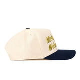 A side view of the No Rivals Michigan Wolverines Script Overlay Hat shows its cream-colored crown and navy blue brim. Partially visible yellow embroidered text on the front panel highlights its officially licensed design.