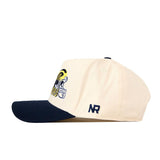 A cream-colored snapback hat with a navy blue brim, the No Rivals Michigan Wolverines Script Overlay Hat features an officially licensed football helmet graphic and “NR” embroidered on the side.